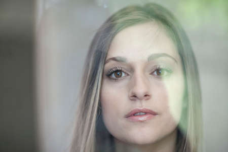 Young woman looking through glass, close-upの写真素材