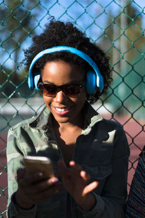 Woman outdoors, wearing headphones, using smartphone