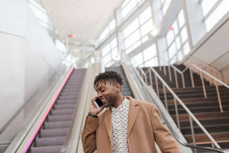Young businessman talking on smartphone moving down train station escalatorの写真素材