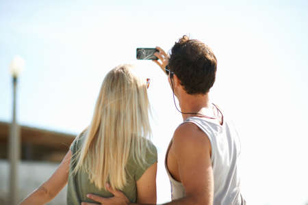 Rear view of couple taking smartphone selfie at Venice Beach, Los Angeles, California, USAの写真素材