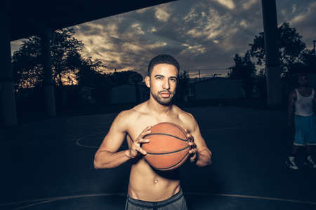 Bare chested man on basketball court holding basketball looking at cameraの写真素材