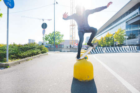 Young male urban skateboarder balancing on top of yellow bollardの写真素材