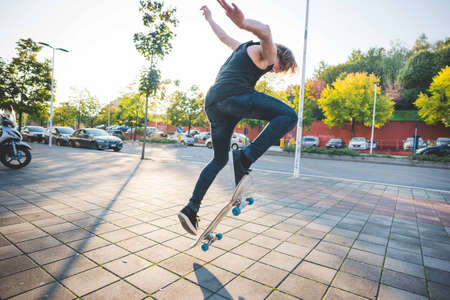 Young male urban skateboarder doing skateboarding jump trick on sidewalkの写真素材