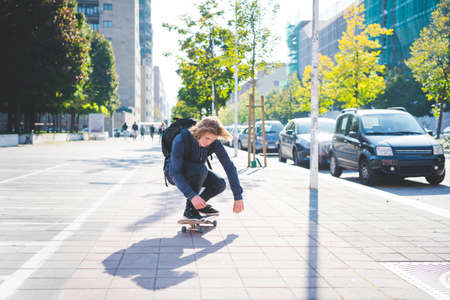 Young male skateboarder crouching whilst skateboarding on sidewalkの写真素材