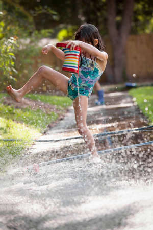 Girl holding welly, jumping over puddle of water on sidewalk