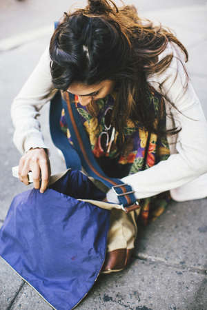 Woman crouching on pavement looking down searching though hip bagの写真素材
