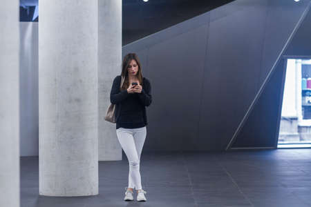 Full length front view of woman standing texting on smartphone