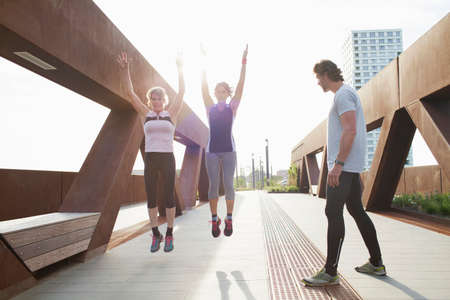 Two women jump training on urban footbridge with male personal trainerの写真素材