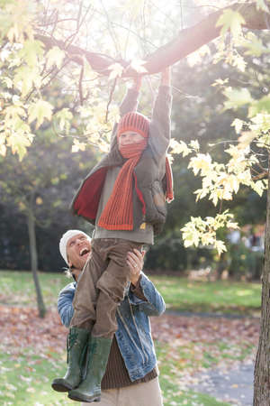 Boy swinging on tree branch, father holding him steady, laughingの写真素材