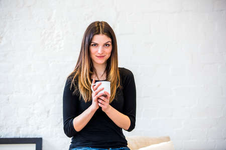 Portrait of beautiful young woman in apartment holding coffee mug
