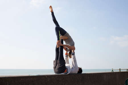 Man and woman practicing acrobatic yoga on wall at Brighton beachの写真素材