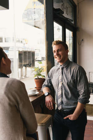 Woman and young man chatting at coffee shop window seatの写真素材