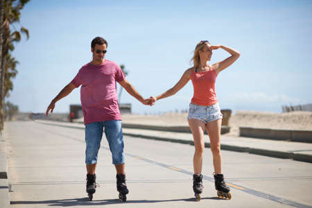 Couple rollerblading outdoors, holding handsの写真素材