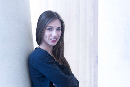 Woman leaning against wall arms crossed looking at camera smiling
