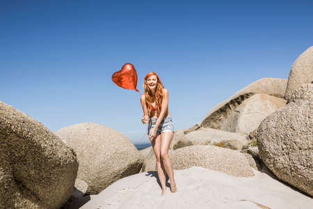 Young woman on beach, holding heart shaped balloonの写真素材