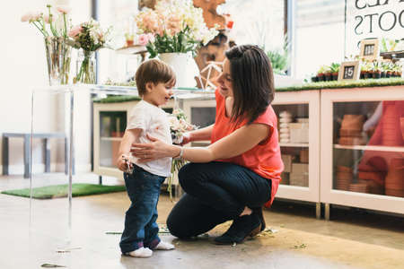 Mother crouching to hug son in flower shopの写真素材