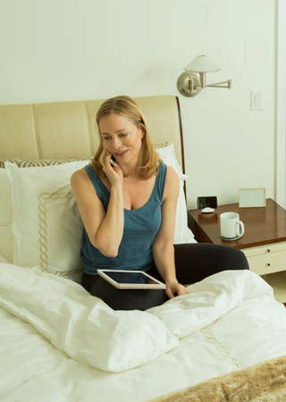 Woman sitting on bed talking on smartphone