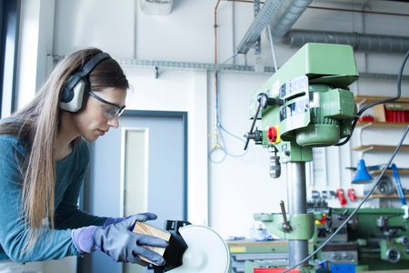 Side view of woman in workshop wearing ear defenders operating belt sanderの写真素材