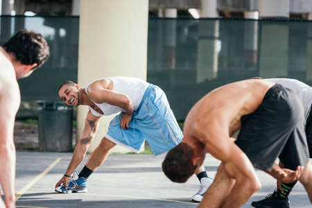 Men on basketball court bending over sideways touching toes smilingの写真素材