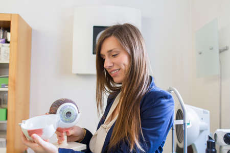 Optician holding anatomical model of eyeball smiling