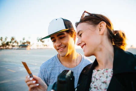 Young couple looking at instant photograph at coast, Venice Beach, California, USA