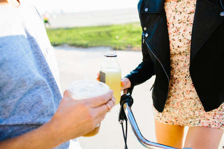 Cropped shot of young couple holding juice and coffee drinks at coastの写真素材