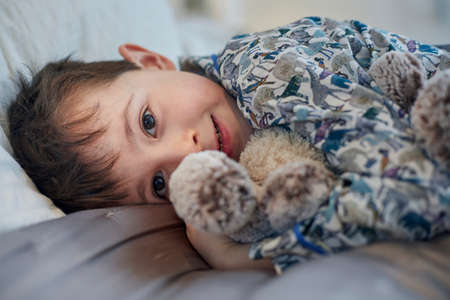 Boy in pyjamas hugging soft toy in bedの写真素材
