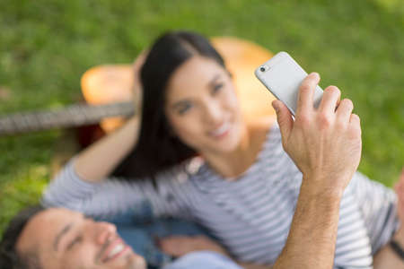 Couple lying on grass using smartphone to take selfieの写真素材