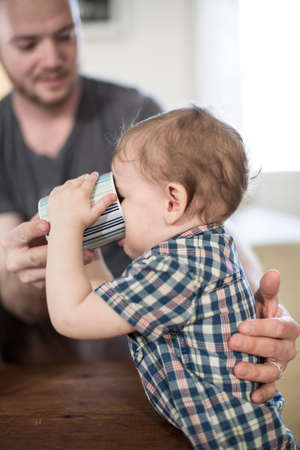 Father helping baby boy to drink from mugの写真素材