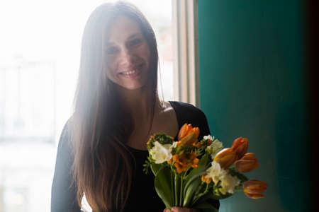 Portrait of young woman at home, holding flowers, smilingの写真素材