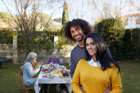 Couple in garden dining with family looking at camera smiling