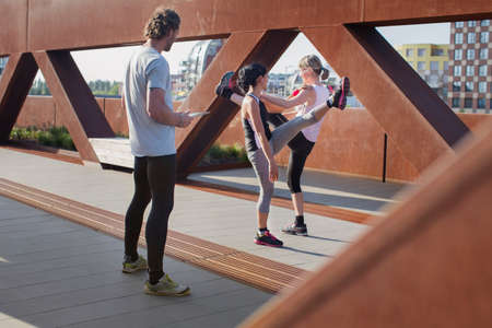 Two women training on urban footbridge with male personal trainer
