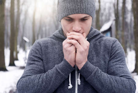 Young man breathing on hands, in snowy forest