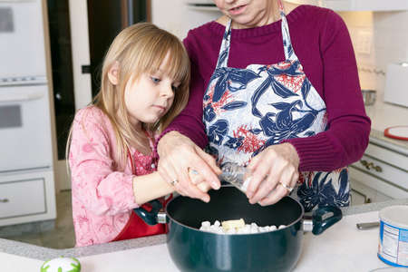 Girl and grandmother measuring salt for saucepanの写真素材