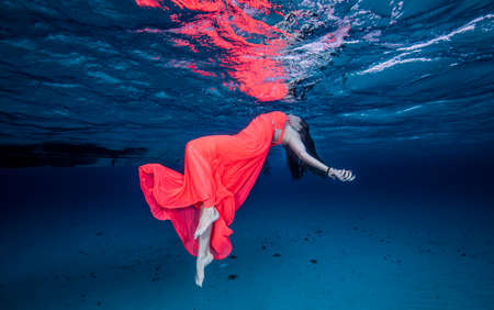 Woman in red floating near surface of oceanの写真素材