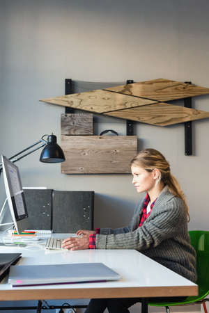 Side view of young woman in office sitting at desk using computer