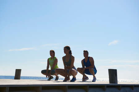 Friends on pier wearing exercise clothes crouching looking away