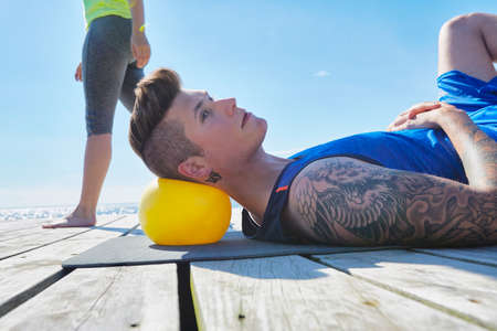 Tattooed man lying on pier using ball as pillowの写真素材