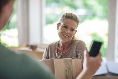 Moving house: woman holding cardboard box, man holding smartphoneの写真素材