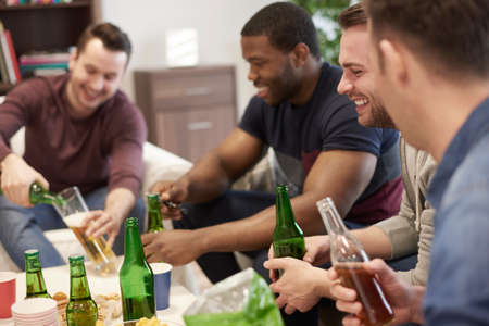 Group of men sitting in lounge holding beer bottles smilingの写真素材
