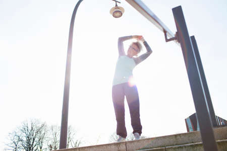 Low angle view of woman on steps arms raised bending over sideways stretchingの写真素材