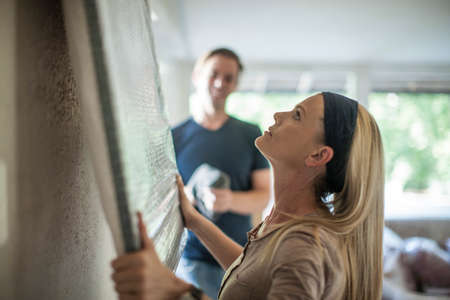 Moving house: woman holding plastic wrapped picture against wallの写真素材