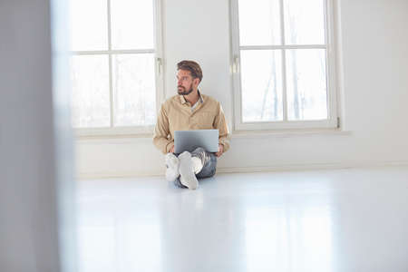 Young man sitting on floor with laptop in empty new home