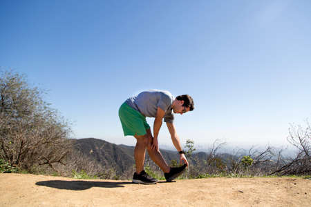 Man on mountain bending forward touching toes stretching footの写真素材