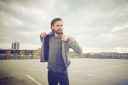 Cool mid adult man putting on jacket at rooftop parking lotの写真素材