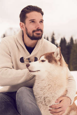Young man petting husky in snow, Elmau, Bavaria, Germanyの写真素材
