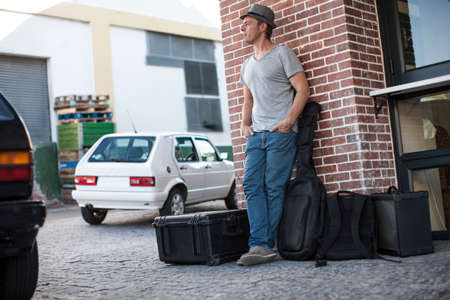 Street musician with musical equipment, standing, leaning against wallの写真素材