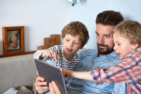 Father and sons on sofa using digital tablet