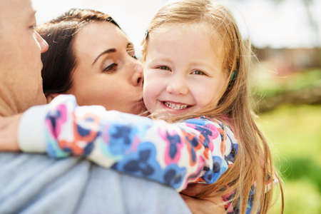 Over shoulder view of mother kissing smiling daughter on cheekの写真素材