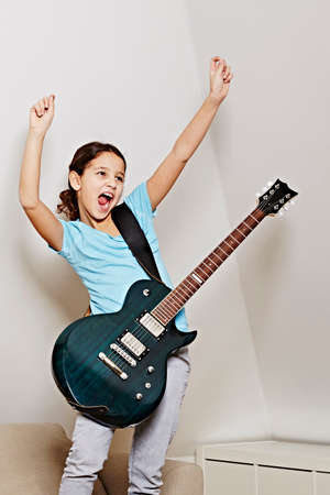 Girl with guitar, mouth open, arms raised in triumphの写真素材